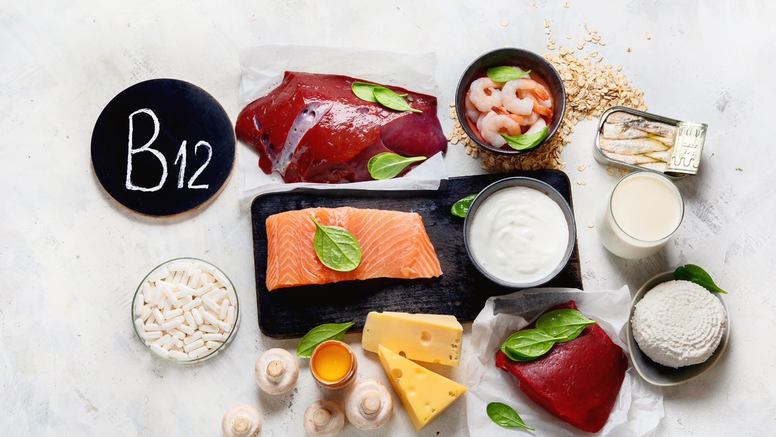 Selezione di alimenti che contengono vitamina b12 come fegato, salmone, uova, formaggi e integratori su un fondo chiaro.